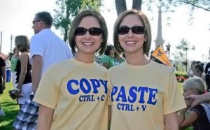 Identical twins are wearing the same yellow t-shirts. One shirt says copy the other says paste.