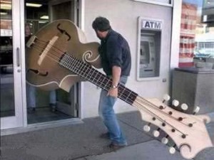 A man carrying a very big guitar into a shop.