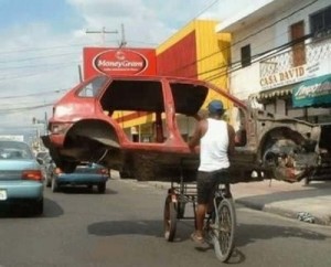 make or do english grammar Man on a bike carrying a half-finished car that he is making.