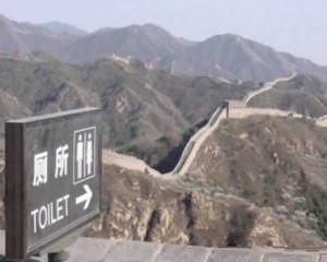 The Great Wall of China disappearing into the distance with a sign for a toilet pointing in the same direction.