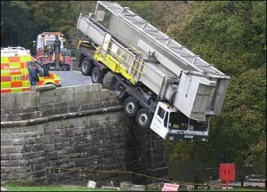 using they instead of he or she A large lorry is hanging over the side of a bridge in English village.